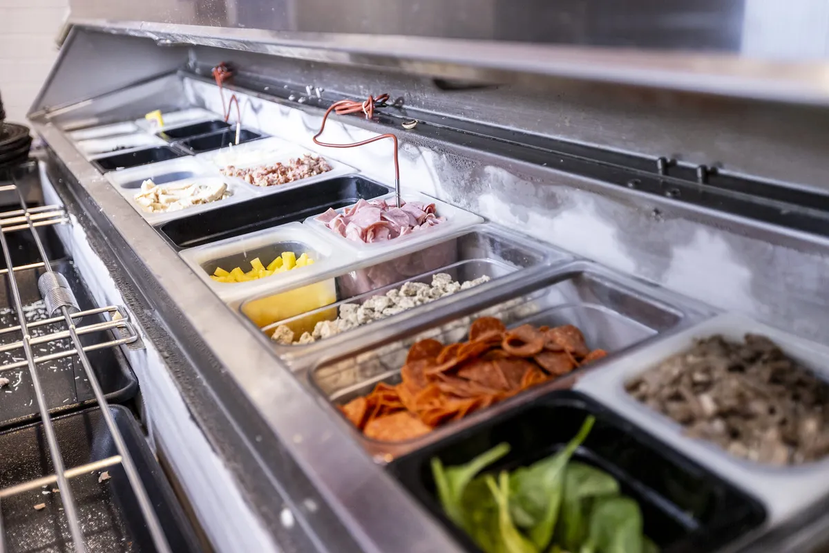 Refrigerated prep-station insert filled with pizza toppings in stainless pans